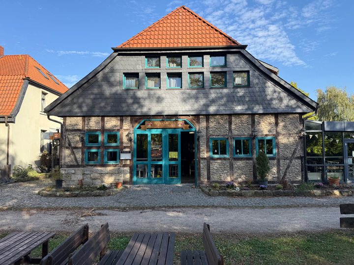 Außenansicht des Wirtshaus am Hasselbach in Wolfsburg: Fachwerkhaus mit Natursteinwänden, rotem Ziegeldach und türkisfarbenen Fenstern und Türen